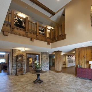 A spacious hotel lobby featuring wooden accents, stone pillars, and a balcony.