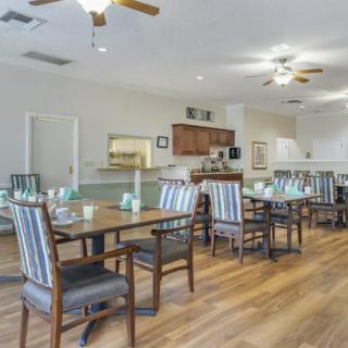A spacious dining room with wooden floors and striped chairs, featuring a kitchen area in the background.