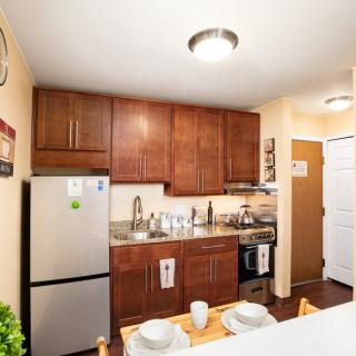A modern apartment kitchen with wooden cabinets and a compact dining area.