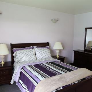 A cozy bedroom with a neatly made bed, bedside lamps, and a mirror.