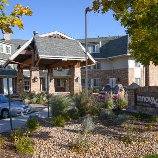 An exterior view of a senior living facility entrance surrounded by landscaped greenery.
