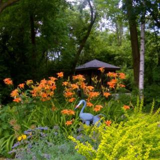 A serene garden scene with vibrant orange lilies, a bird sculpture, and lush greenery.