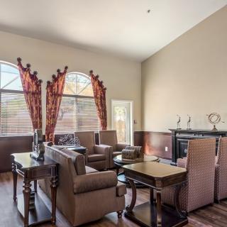 A cozy living room with high ceilings, featuring comfortable seating, a fireplace, and large windows with decorative curtains.