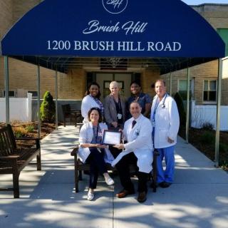 A group of medical professionals posing outside a hospital building under an awning at 1200 Brush Hill Road.