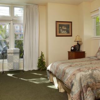 A cozy bedroom with a large bed, nightstand, and windows letting in natural light.