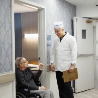 A doctor conversing with a patient in a wheelchair in a hospital corridor.