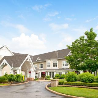 Elegant residential building with a circular driveway and lush greenery.