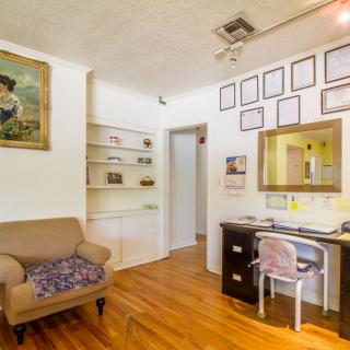 A cozy living room with an office space featuring a desk and chair, decorated with artwork and framed pictures.