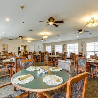 A spacious dining room with neatly arranged tables and chairs, featuring ceiling fans and ample lighting.