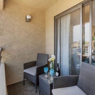 A cozy balcony with two chairs, a small table with wine and glasses, and a decorative vase of flowers.