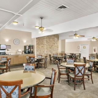 A spacious dining area with multiple round tables and chairs arranged neatly under ceiling fans, featuring a coffee station in the corner.