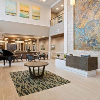 A modern lobby with high ceilings, featuring a piano, artwork on the walls, and comfortable seating arrangements.