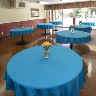 A banquet hall with round tables covered in blue tablecloths, each adorned with a vase of flowers.