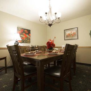A warmly lit dining room featuring a wooden table set for a meal, with a chandelier overhead and artwork adorning the walls.