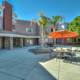 A sunny courtyard with a fountain, outdoor seating, and palm trees in front of a building.