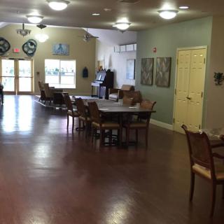 A spacious dining area with multiple tables and chairs on a wooden floor, illuminated by overhead lights.