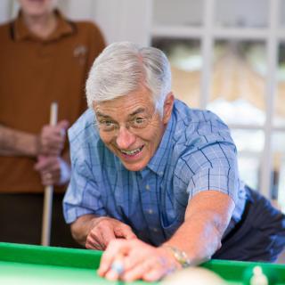A senior man focuses intently as he takes a shot in a game of billiards.