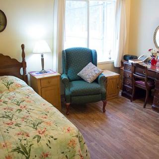 A cozy bedroom with a floral bedspread, armchair, and wooden furniture.