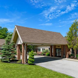 A picturesque building entrance with a covered driveway surrounded by lush greenery and a clear blue sky.