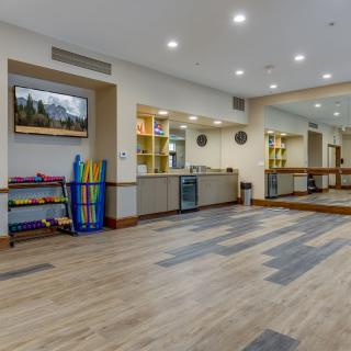 A spacious and well-lit exercise room with wooden flooring, mirrors, and various fitness equipment.