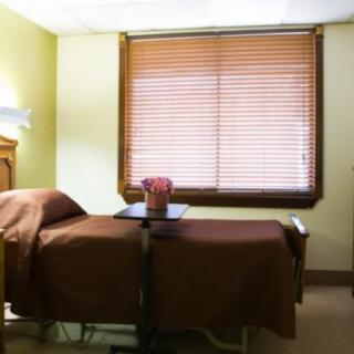 A hospital room with a single bed and adjustable table near the window.