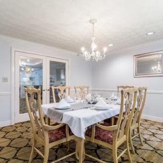 A well-lit dining room featuring a chandelier, a dining table with six chairs, and decorative elements like a mirror and patterned carpet.