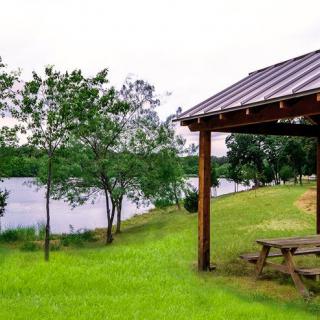 A serene lakeside picnic area with a wooden pavilion and lush green surroundings.