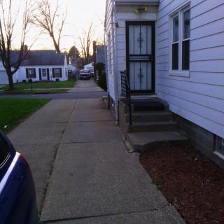 A quiet residential street with a sidewalk and entrance to a house.