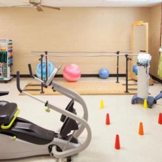 A physical therapy room with exercise equipment including a stationary bike, therapy balls, and cones for rehabilitation exercises.