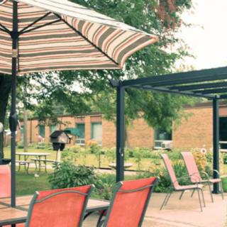 A cozy patio area with red chairs, tables, and a striped umbrella in a garden setting.
