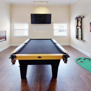 A well-lit game room featuring a billiard table, television, and wooden flooring.