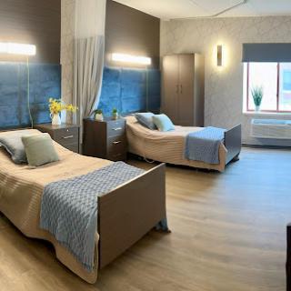A modern, well-lit hospital room featuring two beds with elegant furnishings and a calming color palette.