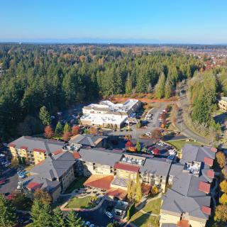An aerial view of a suburban area surrounded by dense forest, showcasing residential buildings and a central facility.