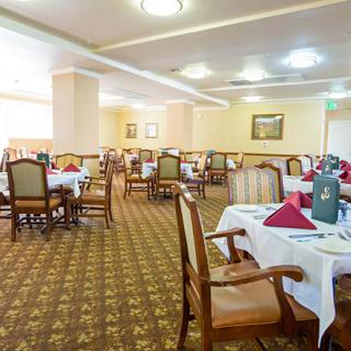 A spacious dining room with neatly arranged tables and chairs, featuring elegant table settings and carpeted flooring.