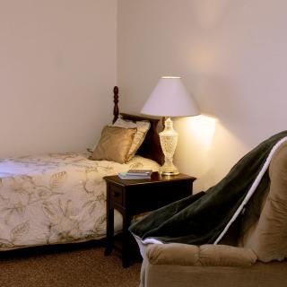 A cozy bedroom with a single bed, nightstand, and chair.