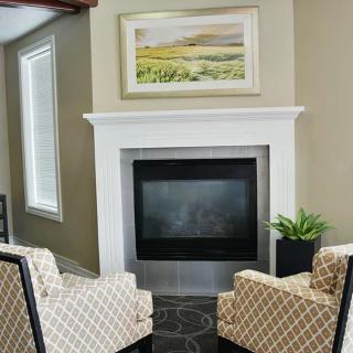 A cozy living room with two patterned armchairs facing a fireplace and a piece of artwork above it.