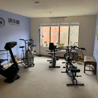 A bright indoor exercise room equipped with stationary bikes and a treadmill.