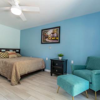 A cozy bedroom with a blue accent wall, featuring a bed, teal chair with matching ottoman, and decorative artwork.