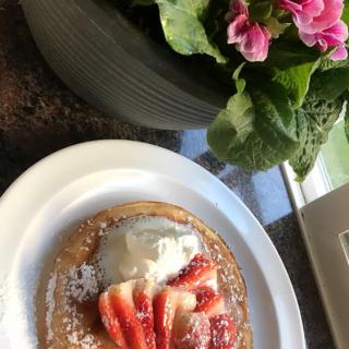 A delicious pancake topped with strawberries, cream, and powdered sugar next to a flower pot.