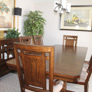 A well-furnished dining room featuring a wooden table and chairs, with decorative plants and artwork.