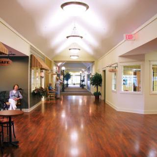 A spacious and well-lit hallway with wooden flooring, featuring seating areas and decorative plants.