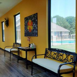 A modern interior waiting area featuring ornate benches, large windows, and bright yellow walls.