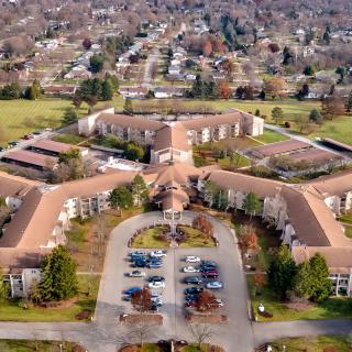 Aerial view of a large building complex situated in a suburban area with surrounding greenery and a parking lot in the foreground.