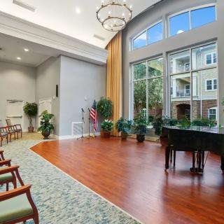 A modern interior space with a grand piano, large windows, and neatly arranged chairs.