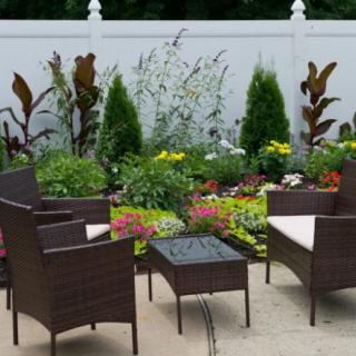 A cozy patio setup with wicker chairs and a table, surrounded by a lush garden filled with various plants and colorful flowers.
