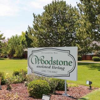 A sign for Woodstone Assisted Living surrounded by a well-maintained lawn and trees.