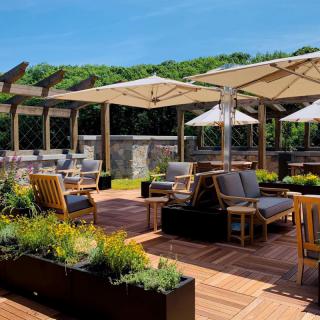 An inviting outdoor patio with comfortable seating, umbrellas, and lush greenery on a sunny day.