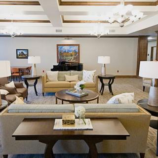 A well-furnished living room featuring sofas, tables, lamps, and a grand piano.