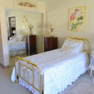 A cozy bedroom featuring a single brass-framed bed with floral bedding, mirrored closet doors, and elegant decor.