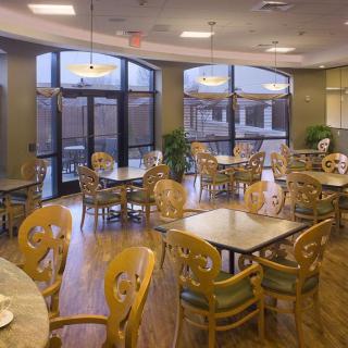 An empty dining area with wooden tables and chairs, featuring large windows.